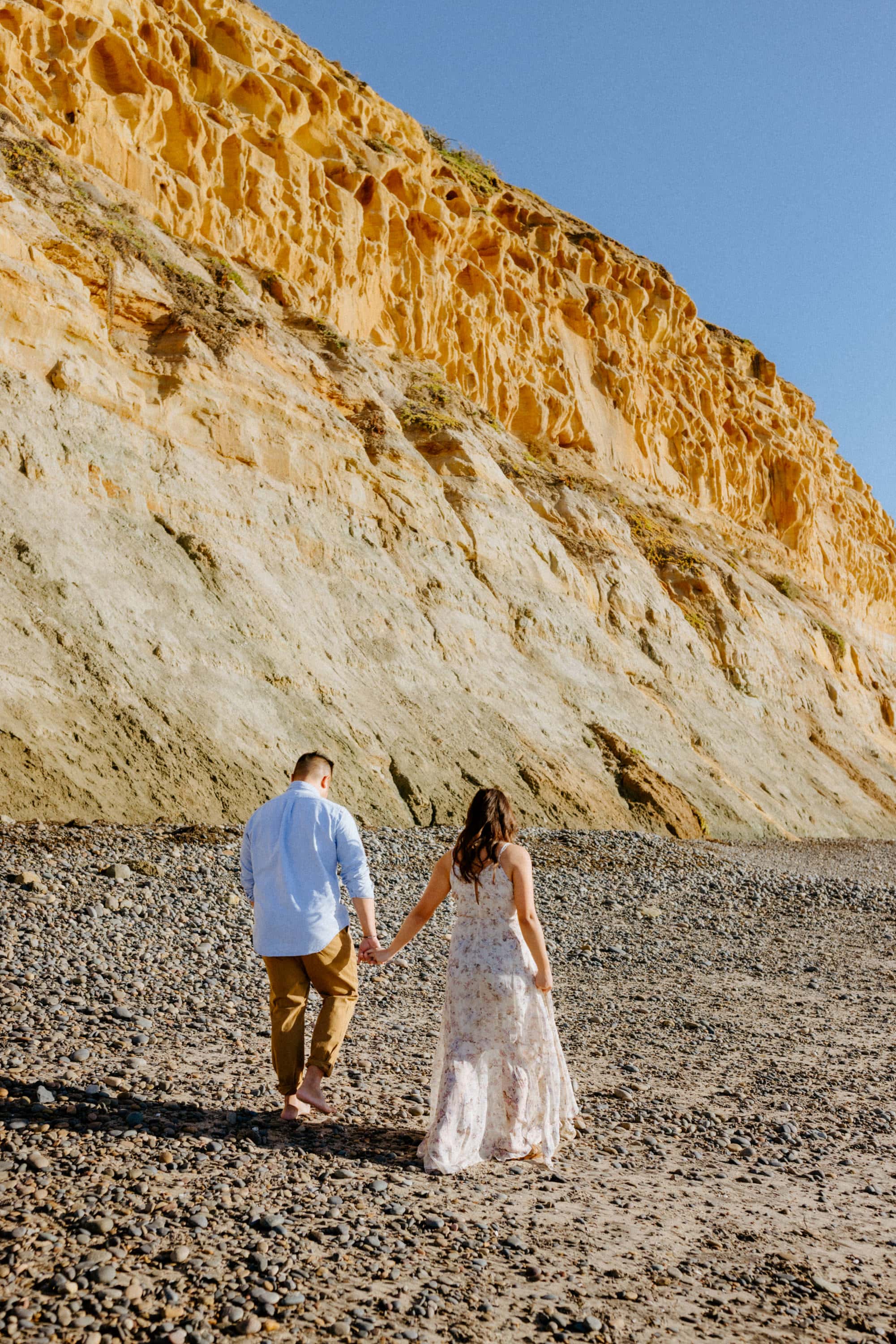 Couple holding hands and walking along the sandy beach at Torrey Pines beach