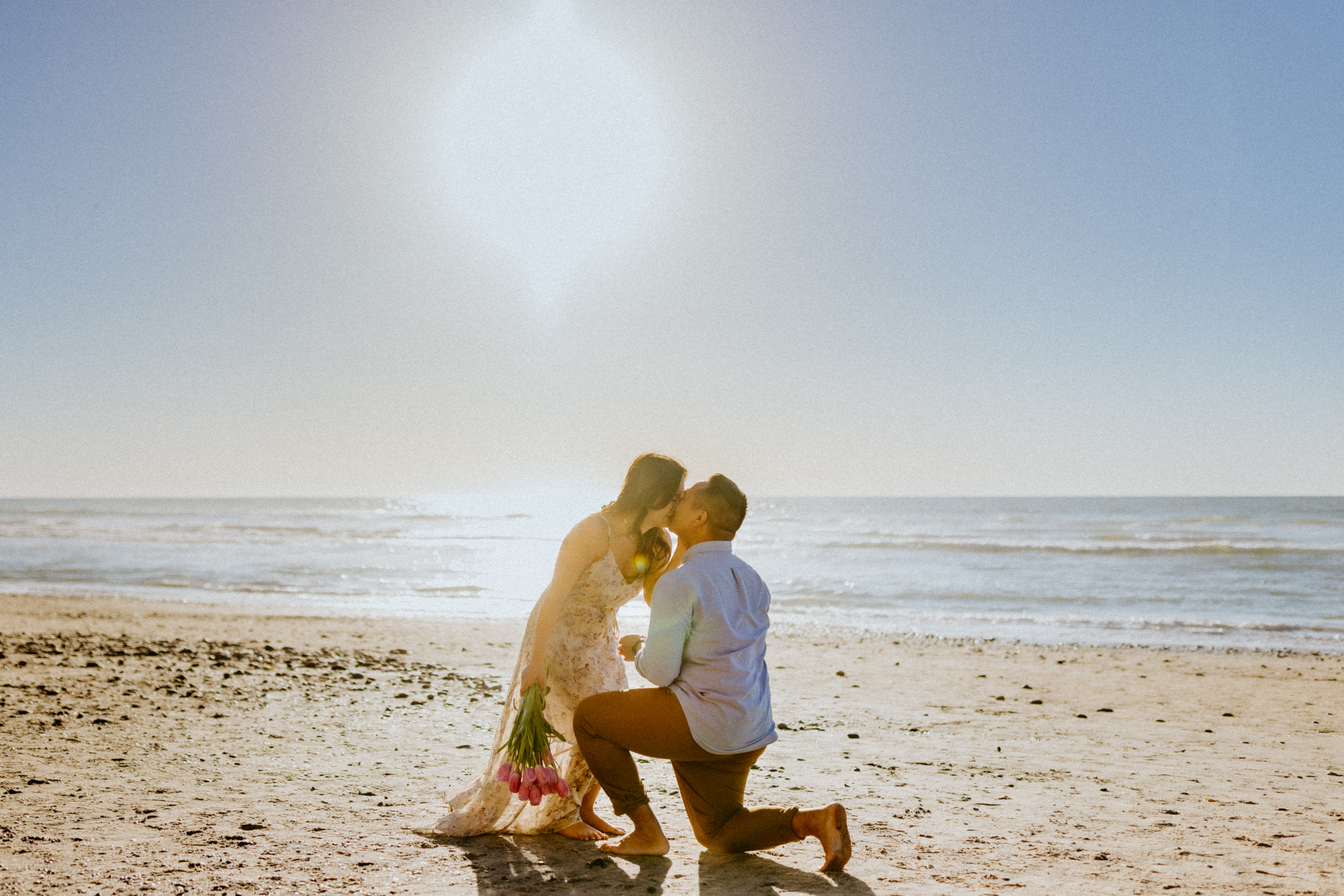 Romantic beach proposal with ocean waves crashing in the background.