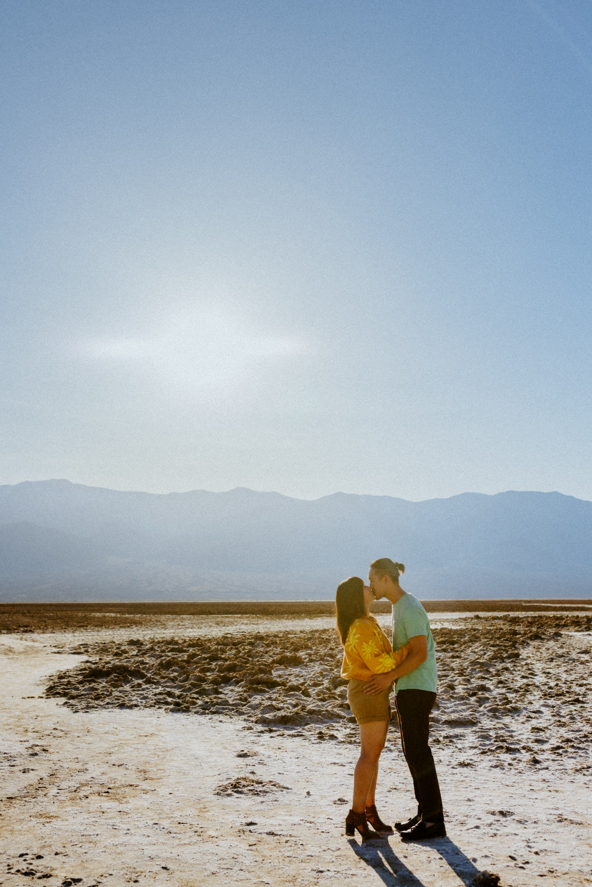 Candid shot of the couple sharing a kiss as they are surrounded by the salt flats for their Death Valley National Park engagement session.